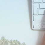 Hands typing on keyboard with palm trees in background