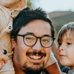 Smiling man with glasses holding two children on each of his shoulders