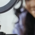 Young woman recording herself with a smartphone on a stand with a ring light on top