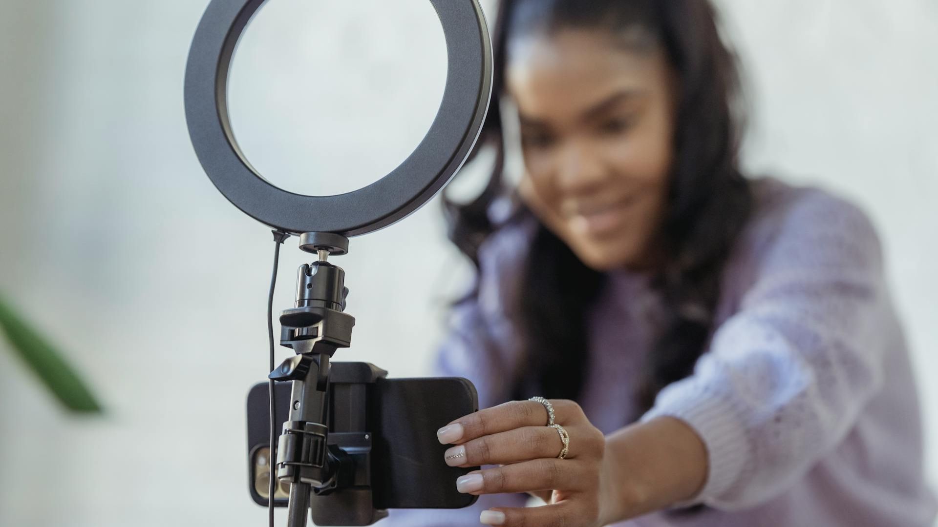 Young woman recording herself with a smartphone on a stand with a ring light on top